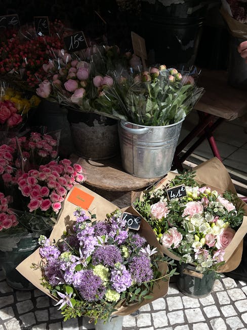 A display of fresh floral arrangements at a flower shop on Marylebone High Street, featuring bouquets with pink roses, purple lilacs, and assorted greenery. The flowers are arranged in various contain