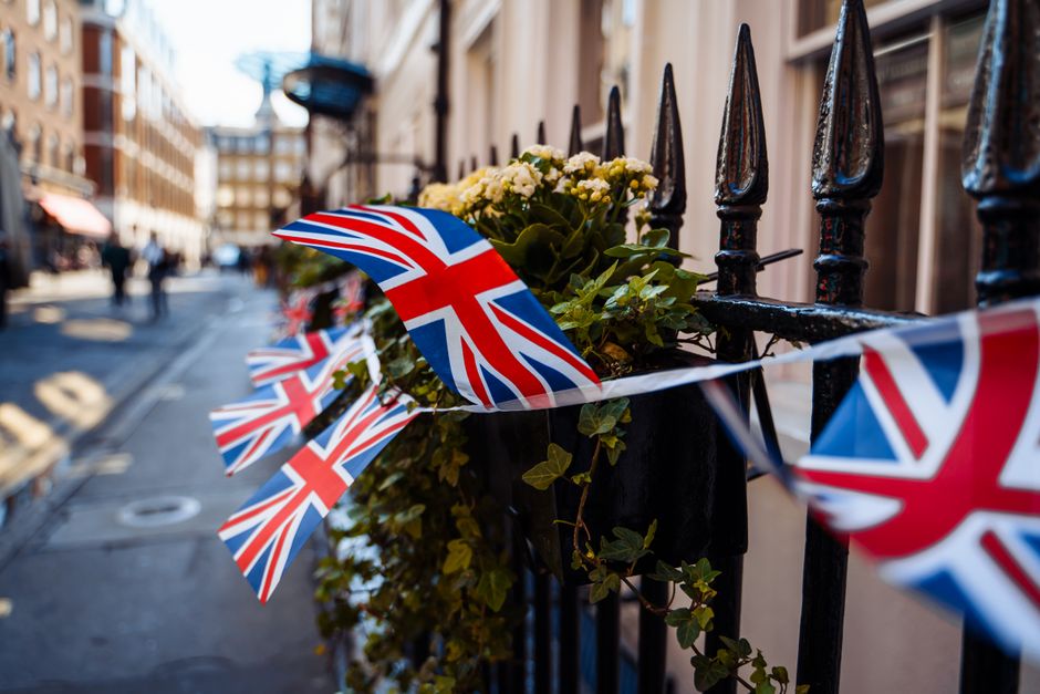 A black wrought iron fence adorned with a bouquet of fresh white and yellow flowers, including daisies and small foliage, wrapped in clear wrapping paper. The flowers are securely placed on top of the